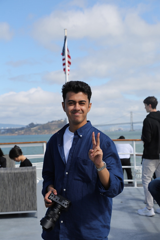 Yash holding a camera on a boat, with the Golden Gate Bridge behind him